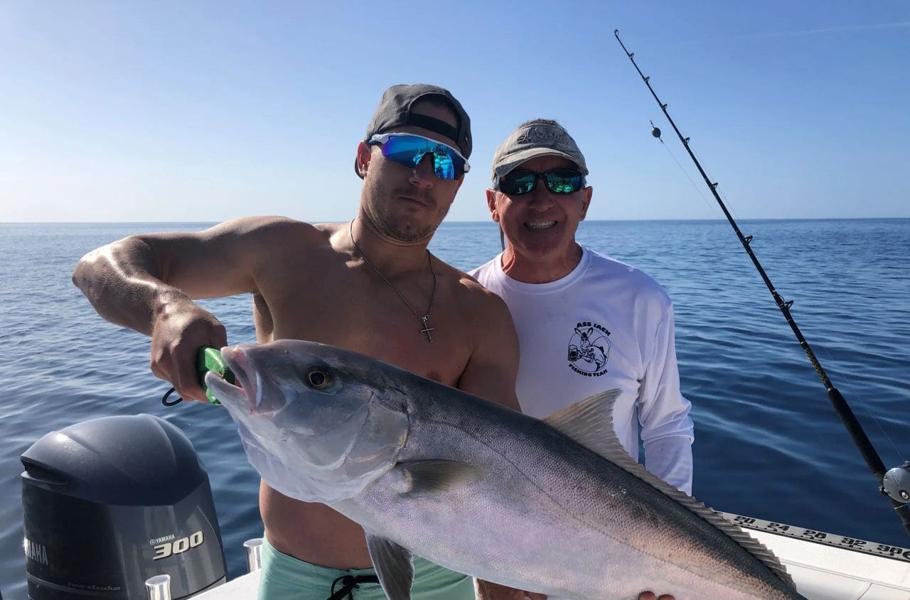 Two men holding a fish on the ocean.